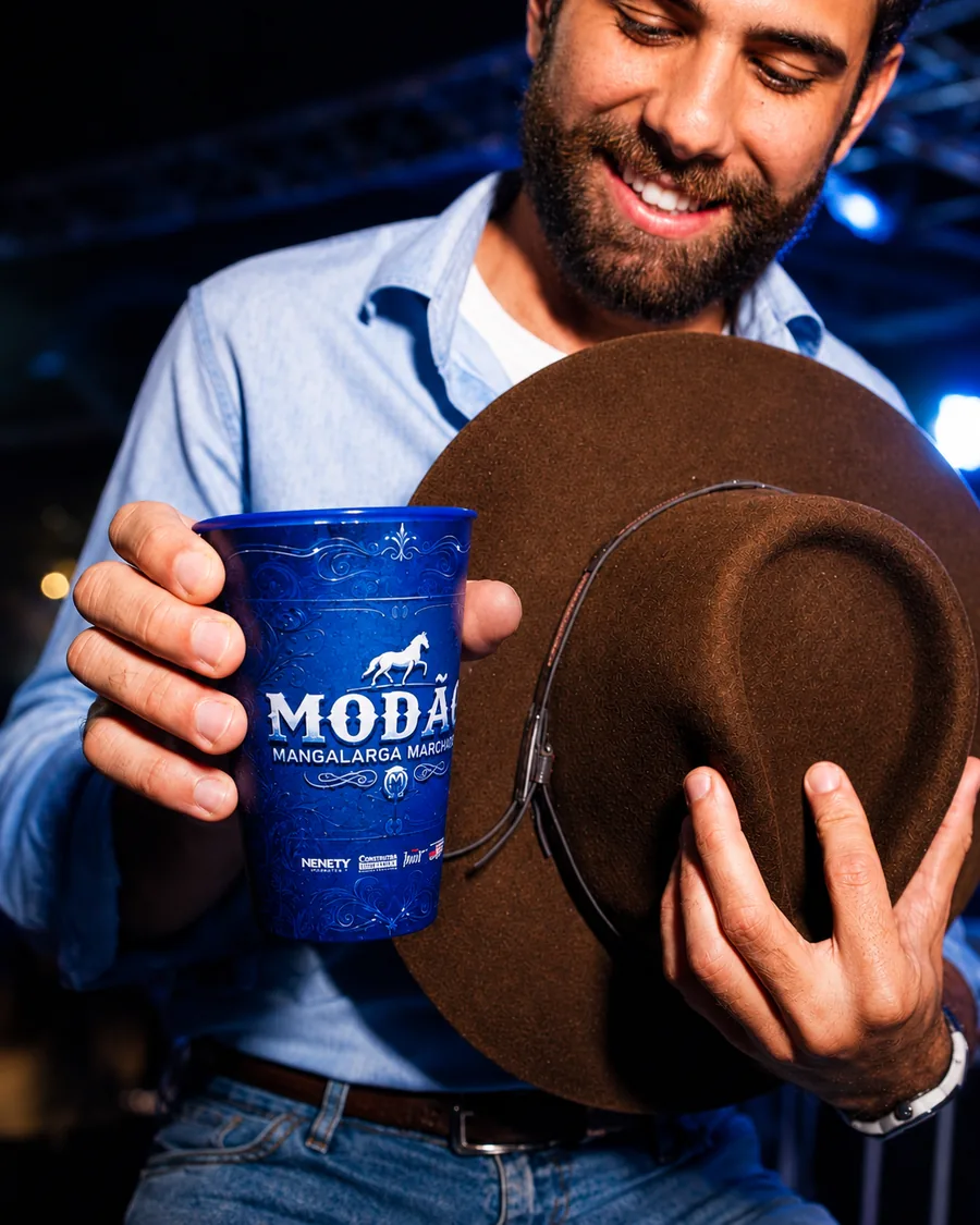 Homem de chapéu segurando um copo azul Modão em uma festa sertaneja